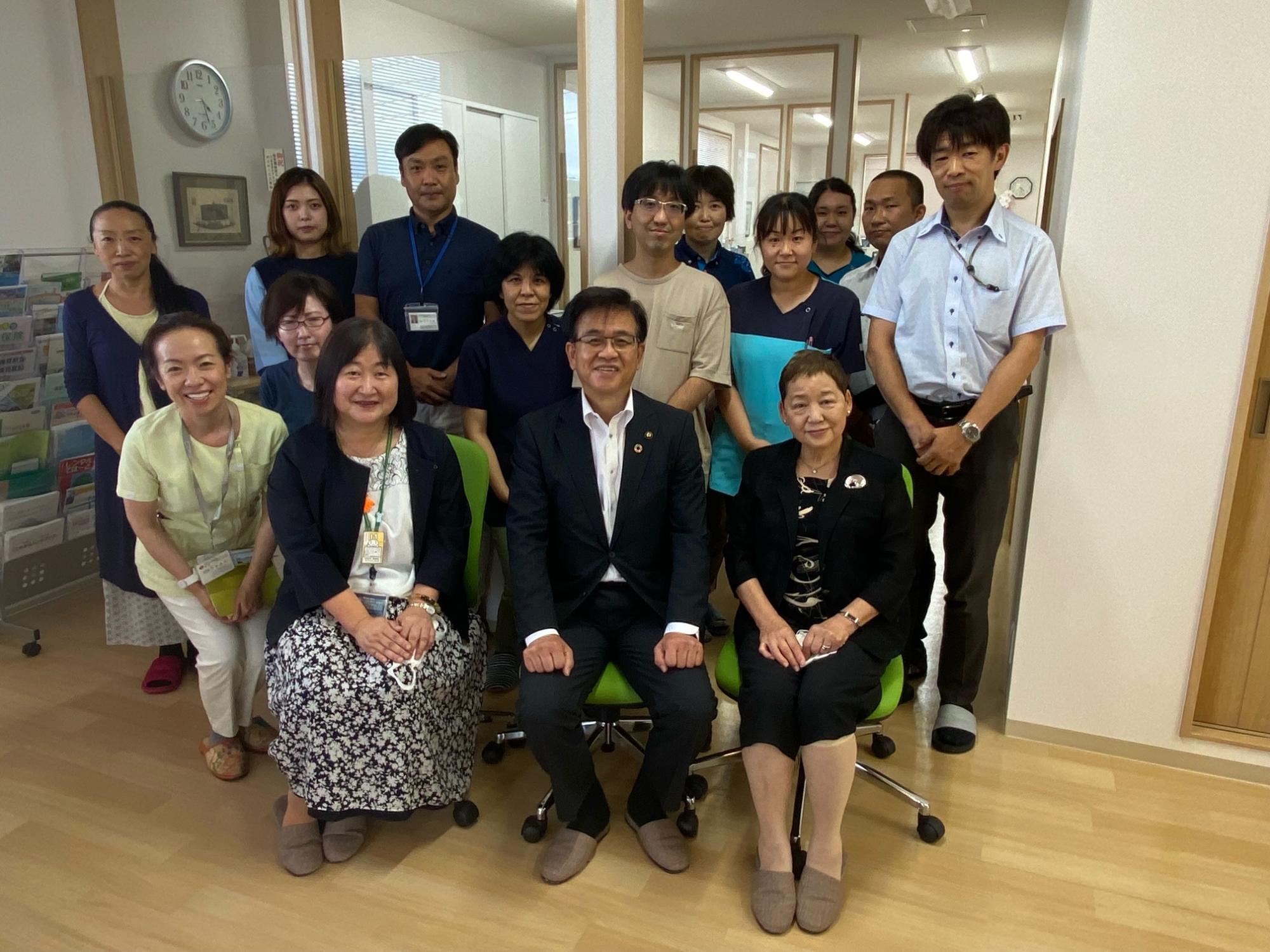 前列に座っている高橋市長を中心に、両側に女性が座り、他の人々が後ろに立って集合写真を撮っている写真