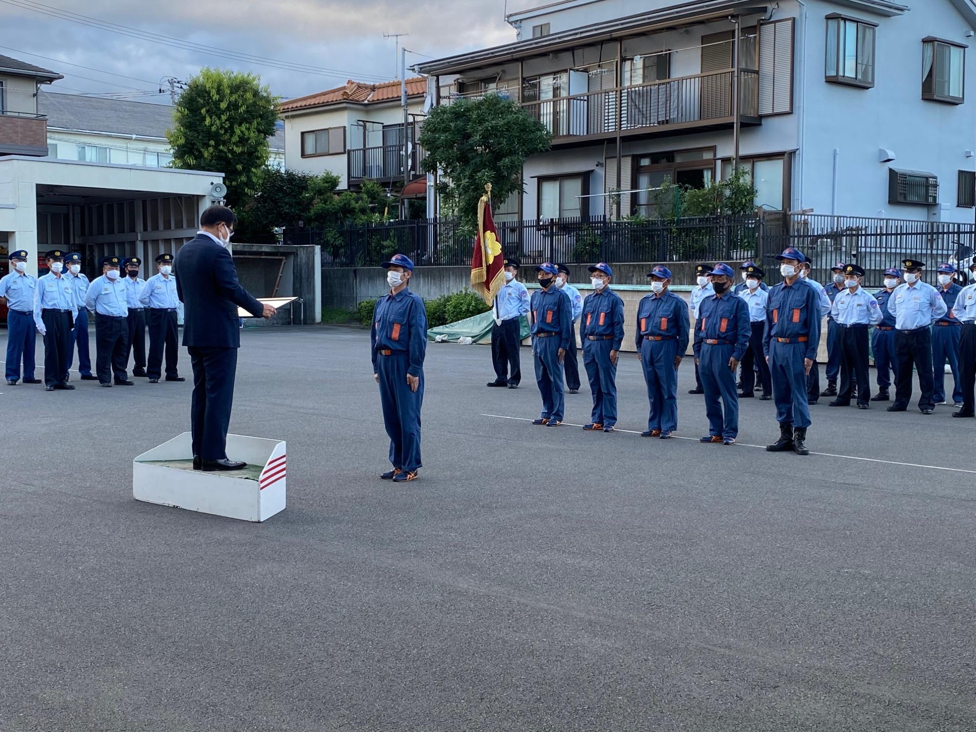 整列している消防団員たちの前に代表の消防団員1名が高橋市長の前に立ち、表彰状を読み上げている高橋市長を見ている写真