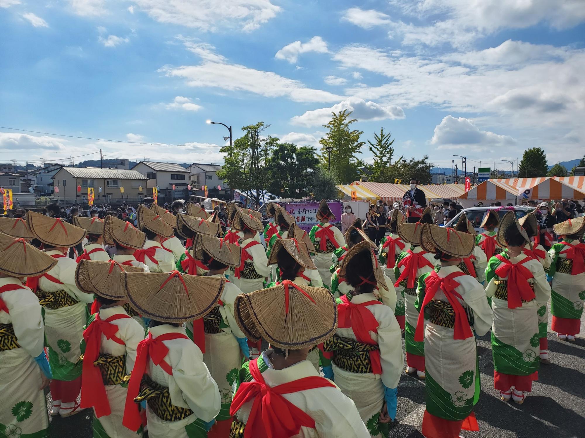 和装に笠をかぶった踊り手たちが、お祭りの会場で、青空の下で一斉に同じ方向を向いて踊っている様子の写真