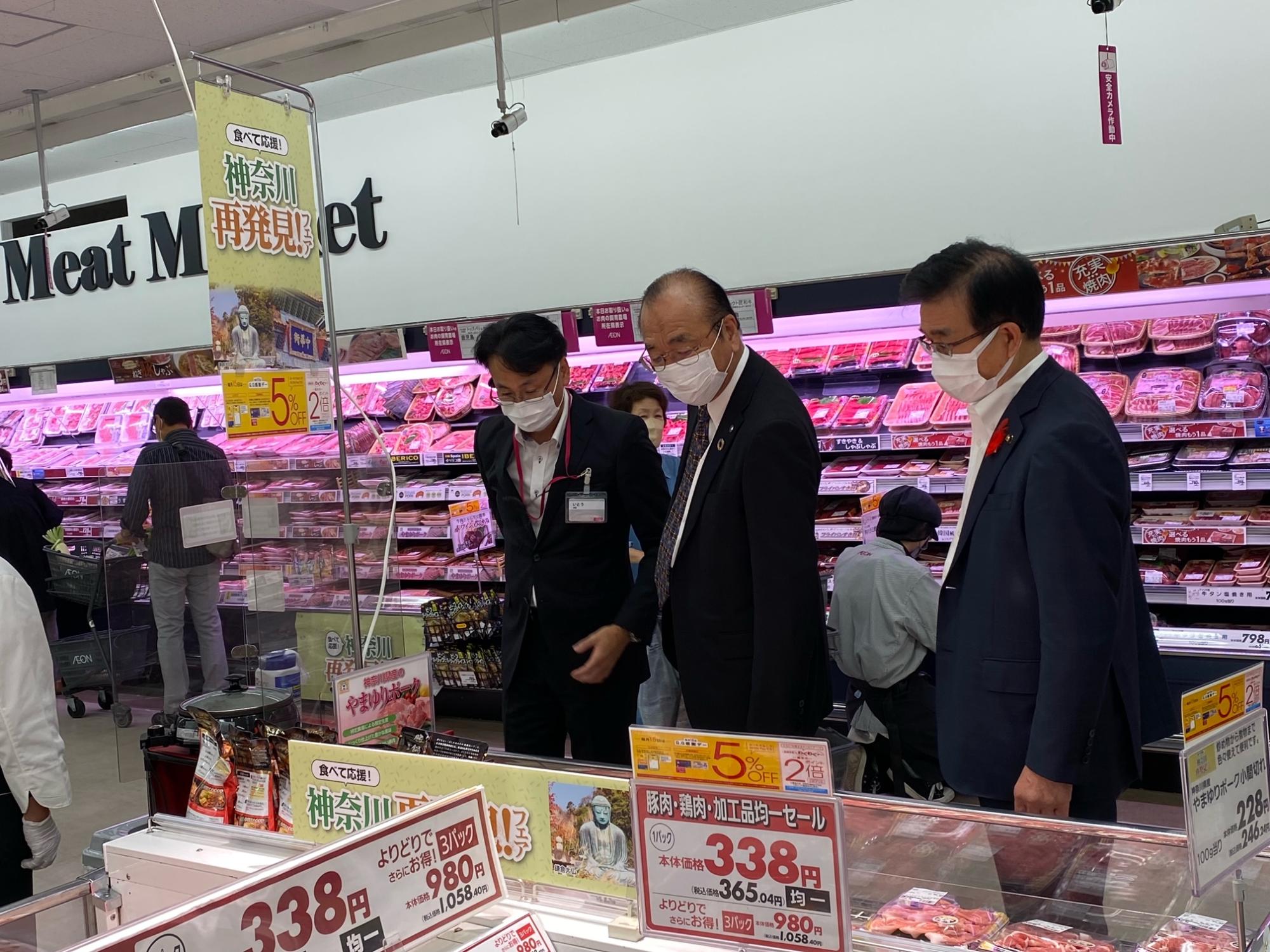 スーパーマーケットの食肉売り場で「神奈川再発見フェア」のポップが掲げられ、スーツ姿の3人の男性がショーケースの中をのぞきこんでいる写真