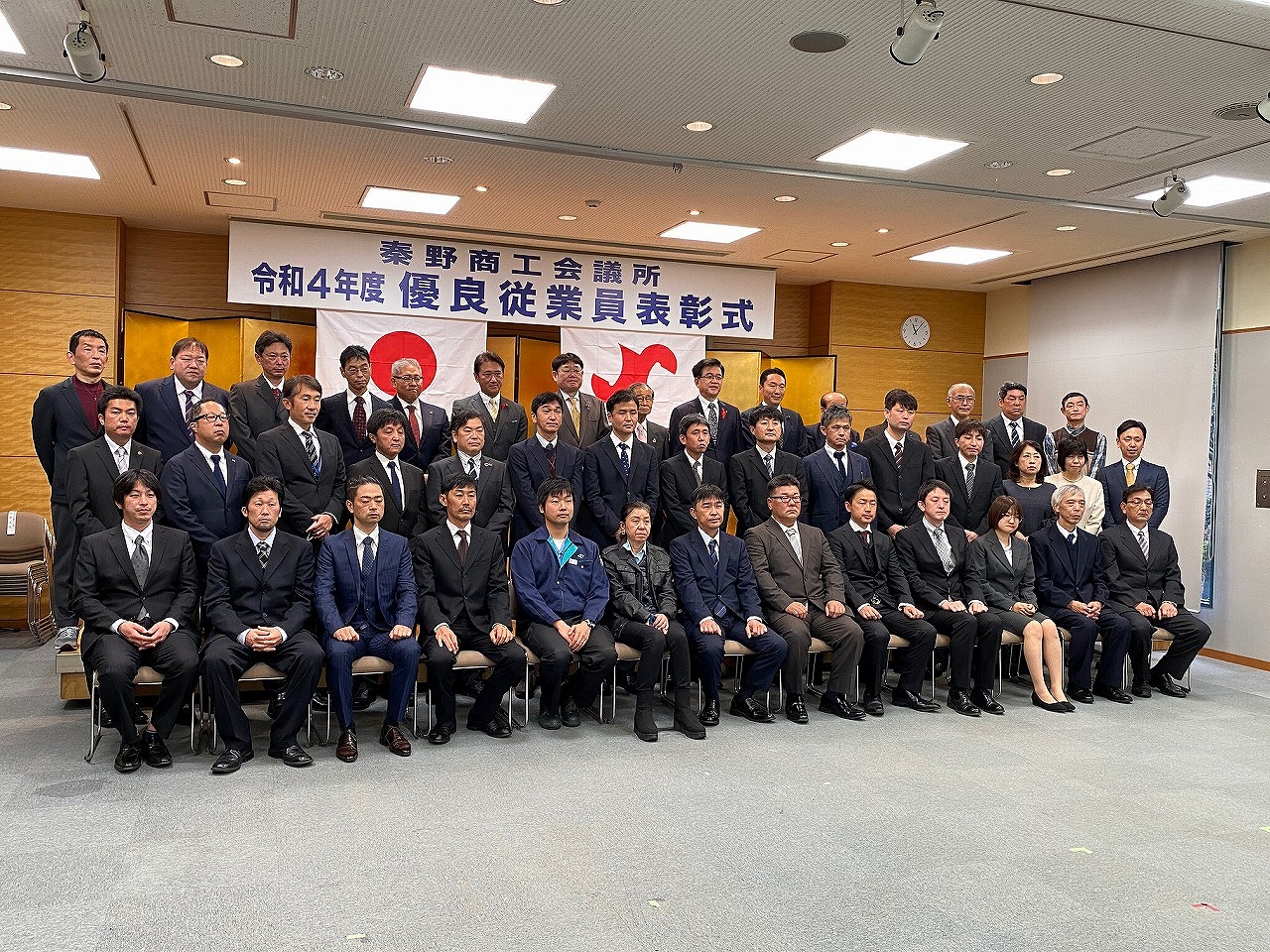 「秦野商工会議所 令和4年度 優良従業員表彰式」と書かれた横断幕の前で、スーツ姿のたくさんの人々が集合写真を撮っている写真