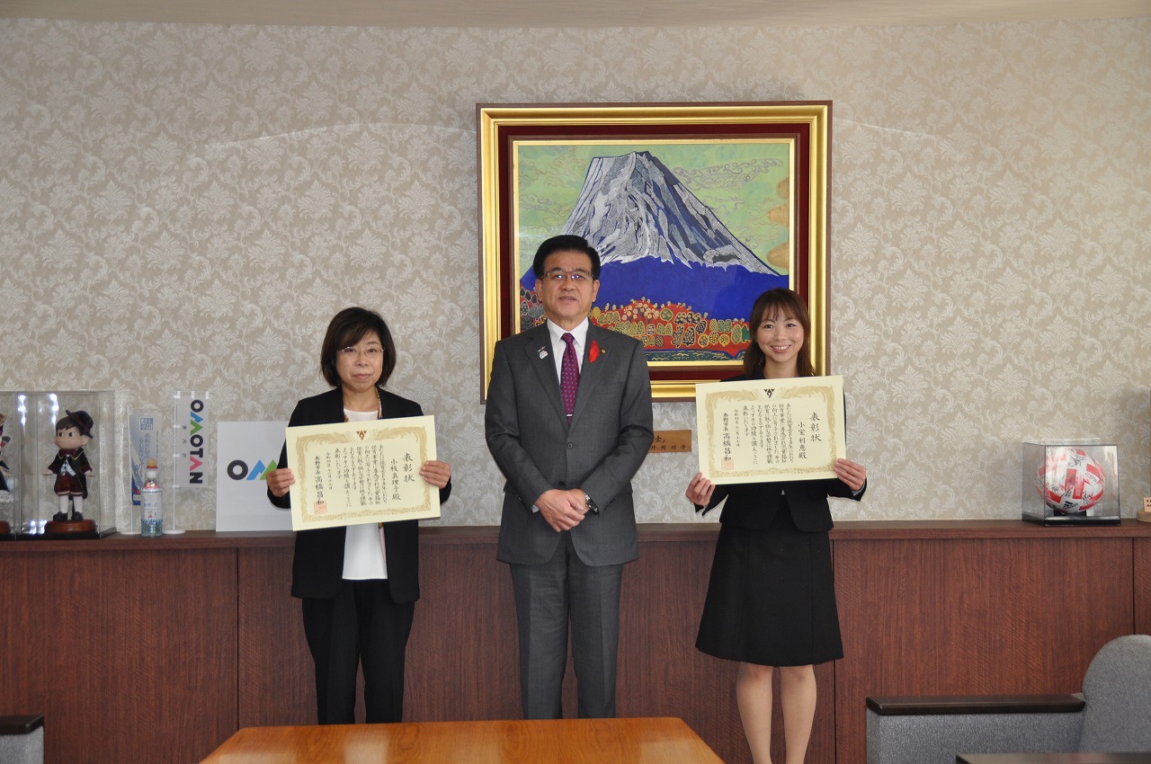スーツ姿の市長が中央に立ち、左右に賞状を持った女性二人が並んで記念撮影をしている写真