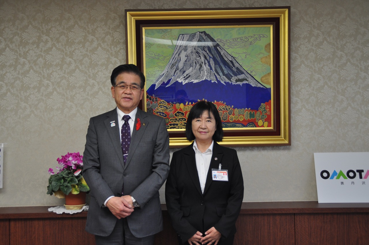 応接室で市長と胸に名札を提げたスーツ姿の女性が並んでおり、二人ともカメラの方を向いている記念写真