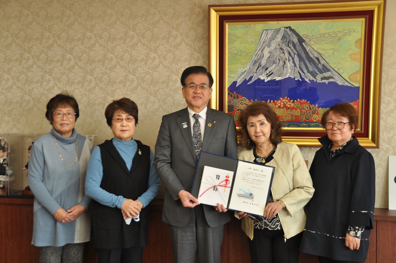 市長を中心にして4人のカラオケ同好会小野教室の方々が立ち、市長と代表の女性が一緒に目録を持って写した記念写真