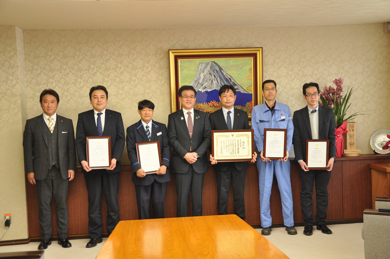 複数のスーツ姿の市長が、各自が額入りの賞状を手にカメラに向かって並び、記念撮影をしている様子の写真