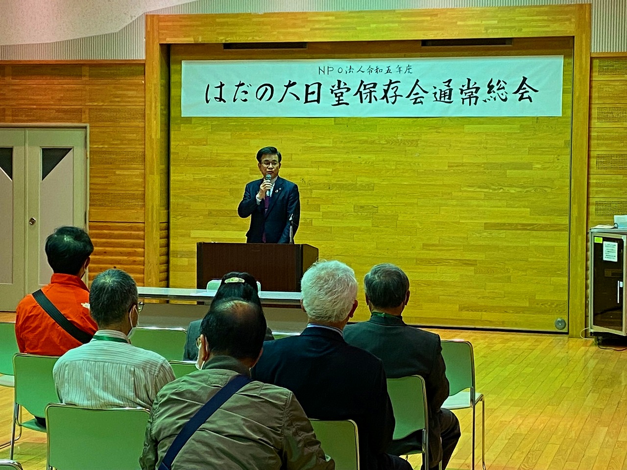 「NPO法人令和五年度 はだの大日堂保存会通常総会」と書かれた横断幕が掲げられた壁を背に、演台に立った高橋市長が椅子に座った複数の出席者に向かってマイクで話をしている写真