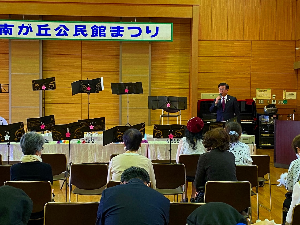 複数の参加者が椅子に座るホールで、「南が丘公民館まつり」と書かれた横断幕の下、ピアノと譜面台が並んでいる前で、高橋市長がマイクを使って挨拶をしている写真