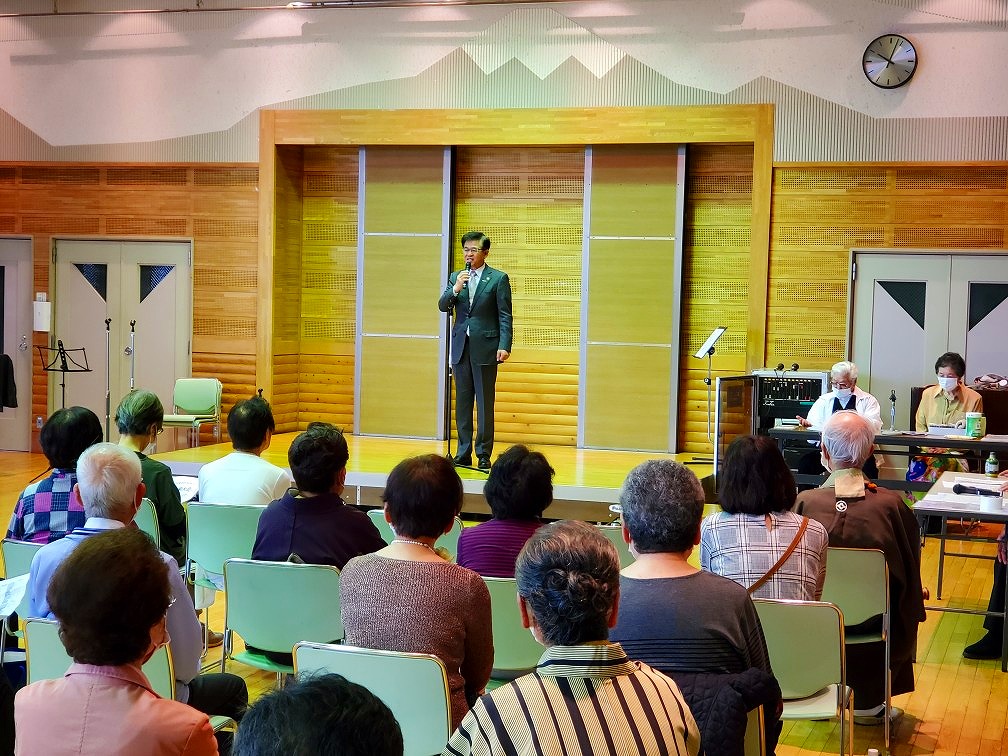 たくさんの出席者が席に座る中、ステージに上がった高橋市長がマイクを持って話をしている様子の写真