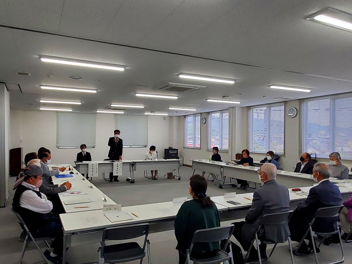 会議室に口の字型にならんだテーブルを囲んでたくさんの出席者が席に座る中、立ち上がった高橋市長がマイクを持って話をしている写真