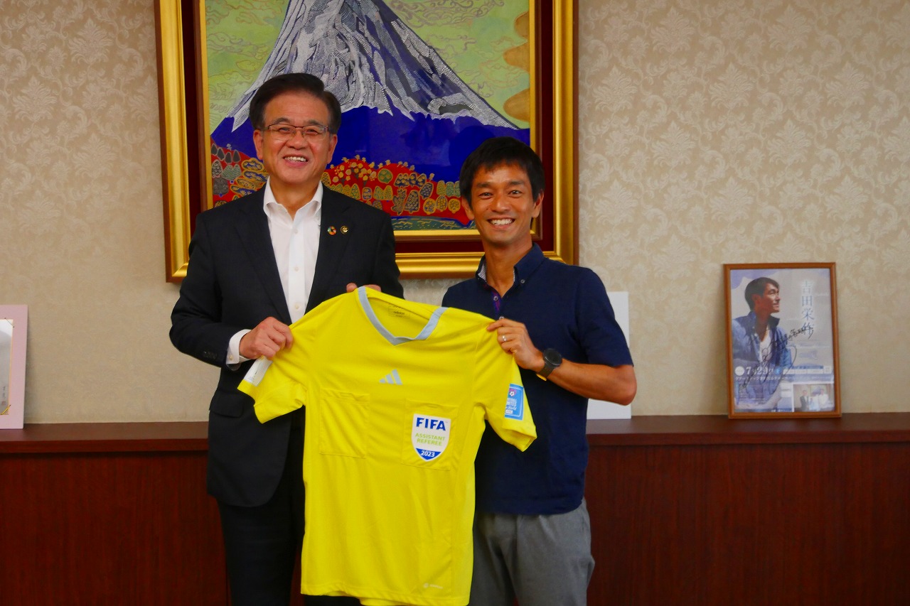 市長と聳城巧さんが二人で黄色のユニフォームを持って記念撮影をしている写真