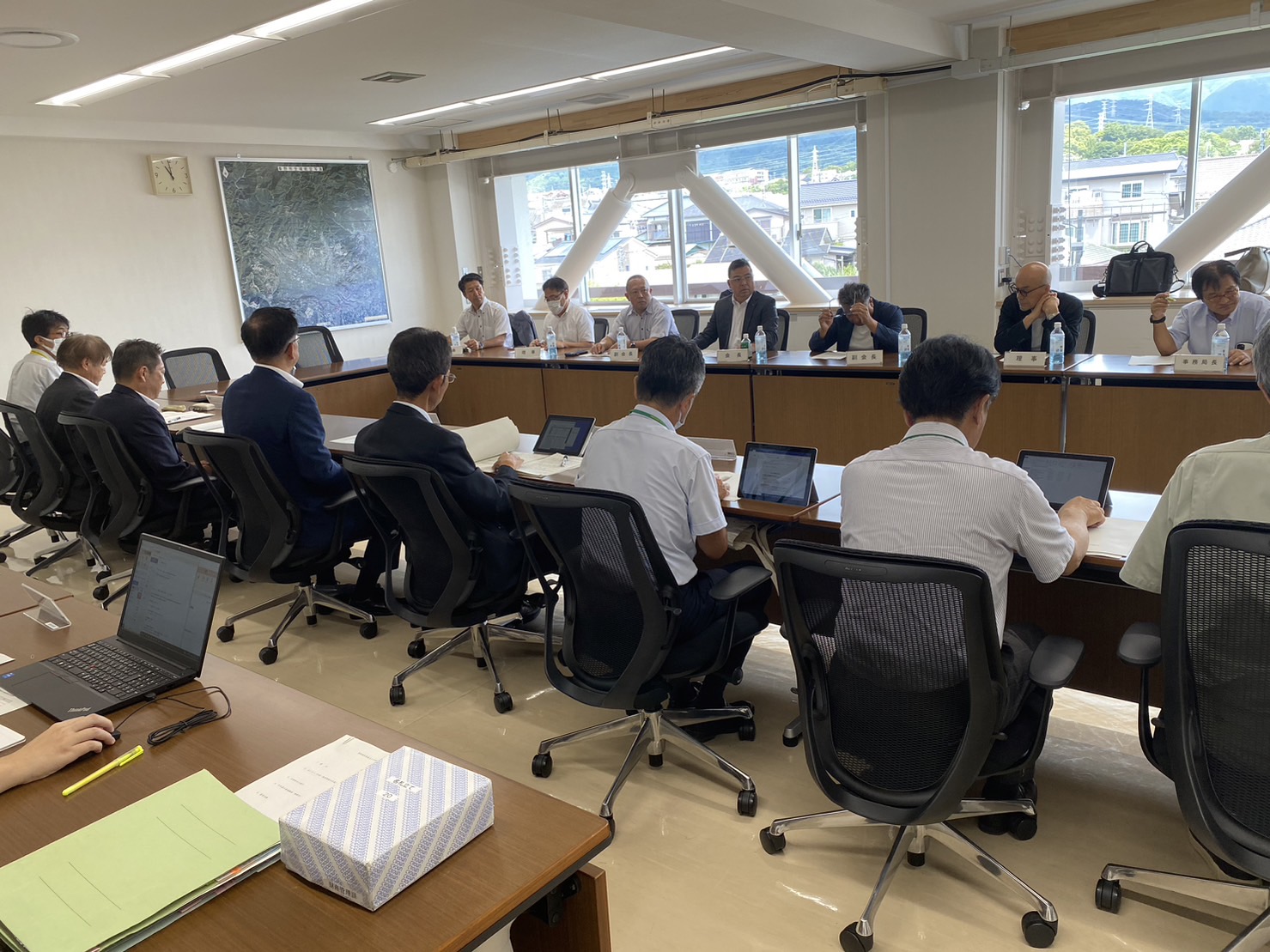 向かい合わせに背t値された机に座った複数の人物が話し合いに参加している意見交換会での写真