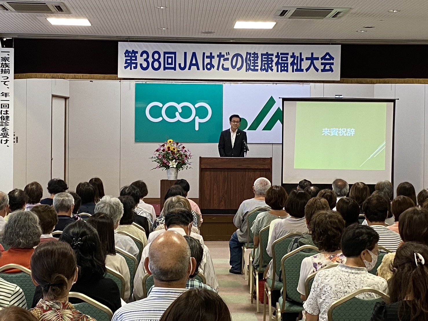 大きな会場で、市長が演台から挨拶をしており、たくさんの聴衆がその話を聞いている第38回JAはだの健康福祉大会の様子の写真