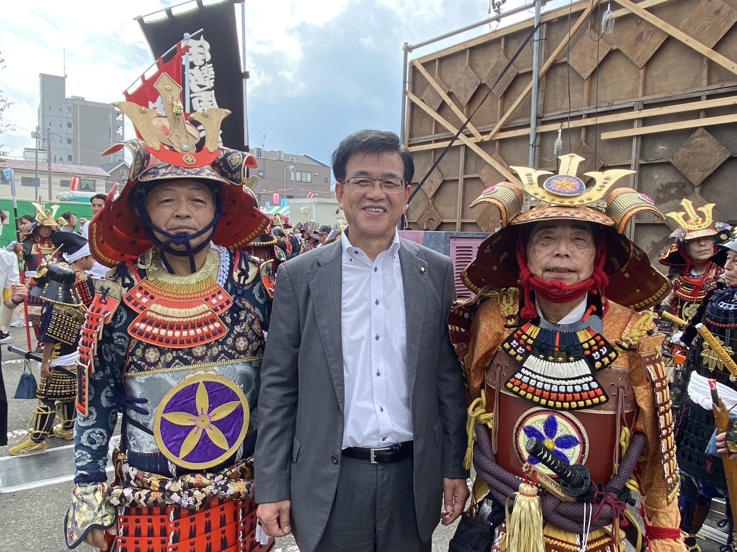 祭りの会場で、甲冑を身につけた2人の男性と、高橋市長が中央で笑顔で並んでいる写真