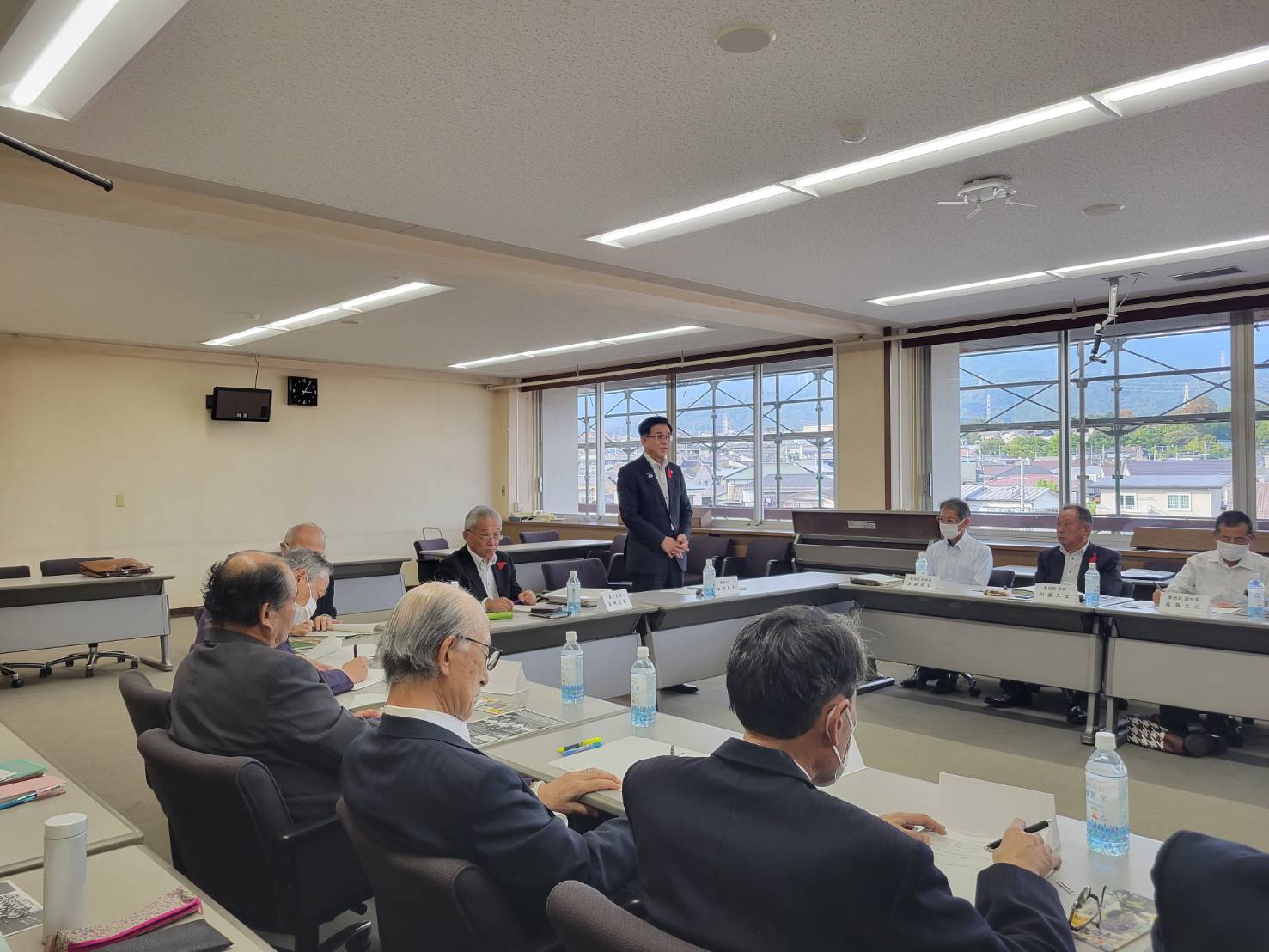 テーブルをコの字型に配置した会議室で、高橋市長が立って話しており、複数の人々が着席して話を聞いている懇親会の写真