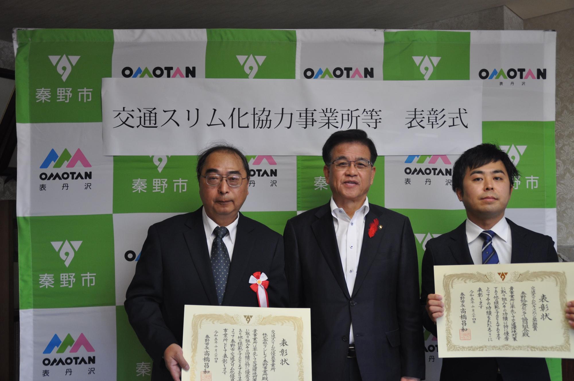 「交通スリム化協力事業所等 表彰式」と書かれた横断幕の前で、中央に立つ高橋市長を囲み、賞状を手に持つ2人の男性が並んでいる記念写真