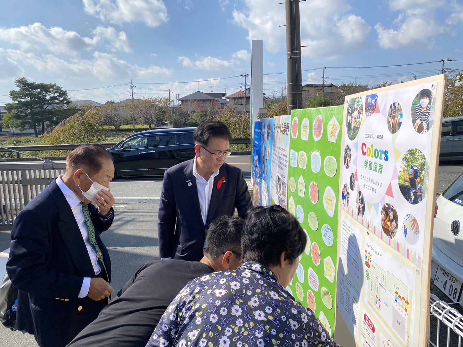 屋外の柵に設置された看板を熱心に見ている高橋市長と関係者の写真