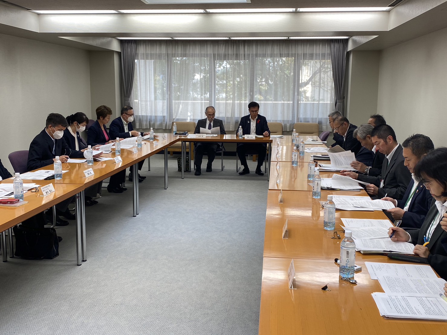 U字型に配置された机に座り、参加者が机の上にある資料を読んでいる様子の写真