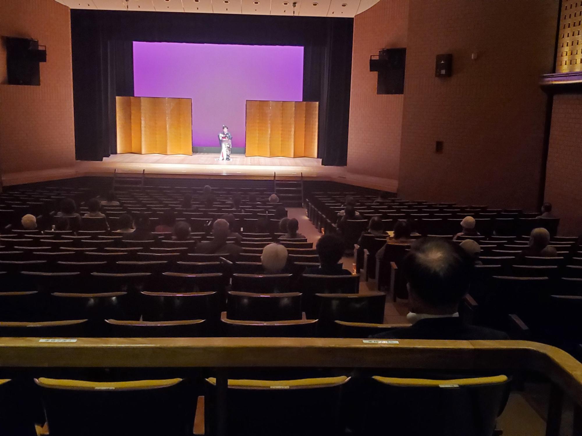 照明が当てられた紫色の背景のステージ全体を客席の後方から移した写真