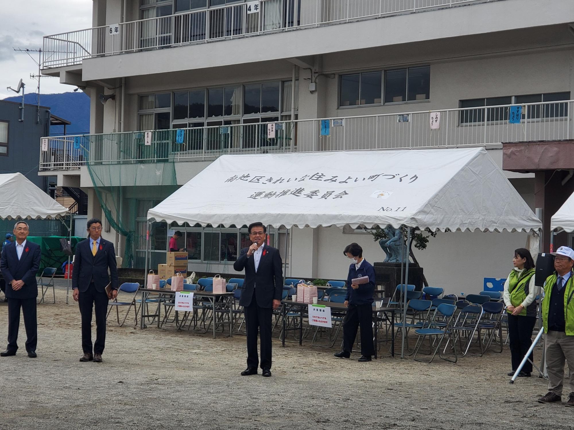 白いテントと椅子が並んだ屋外の広場で、マイクを持って話す高橋市長の写真