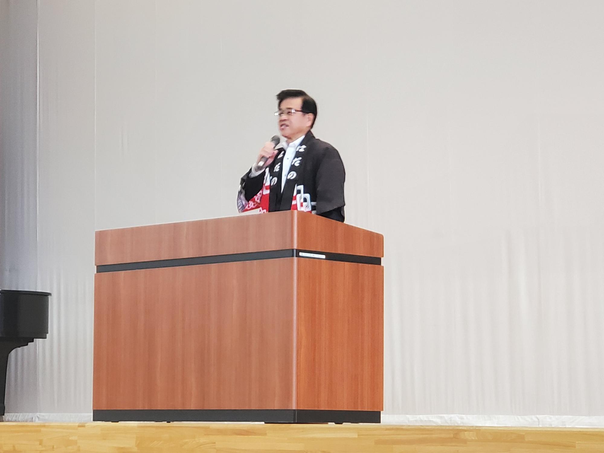 法被姿の高橋市長男性が、壇上でスピーチをしている写真