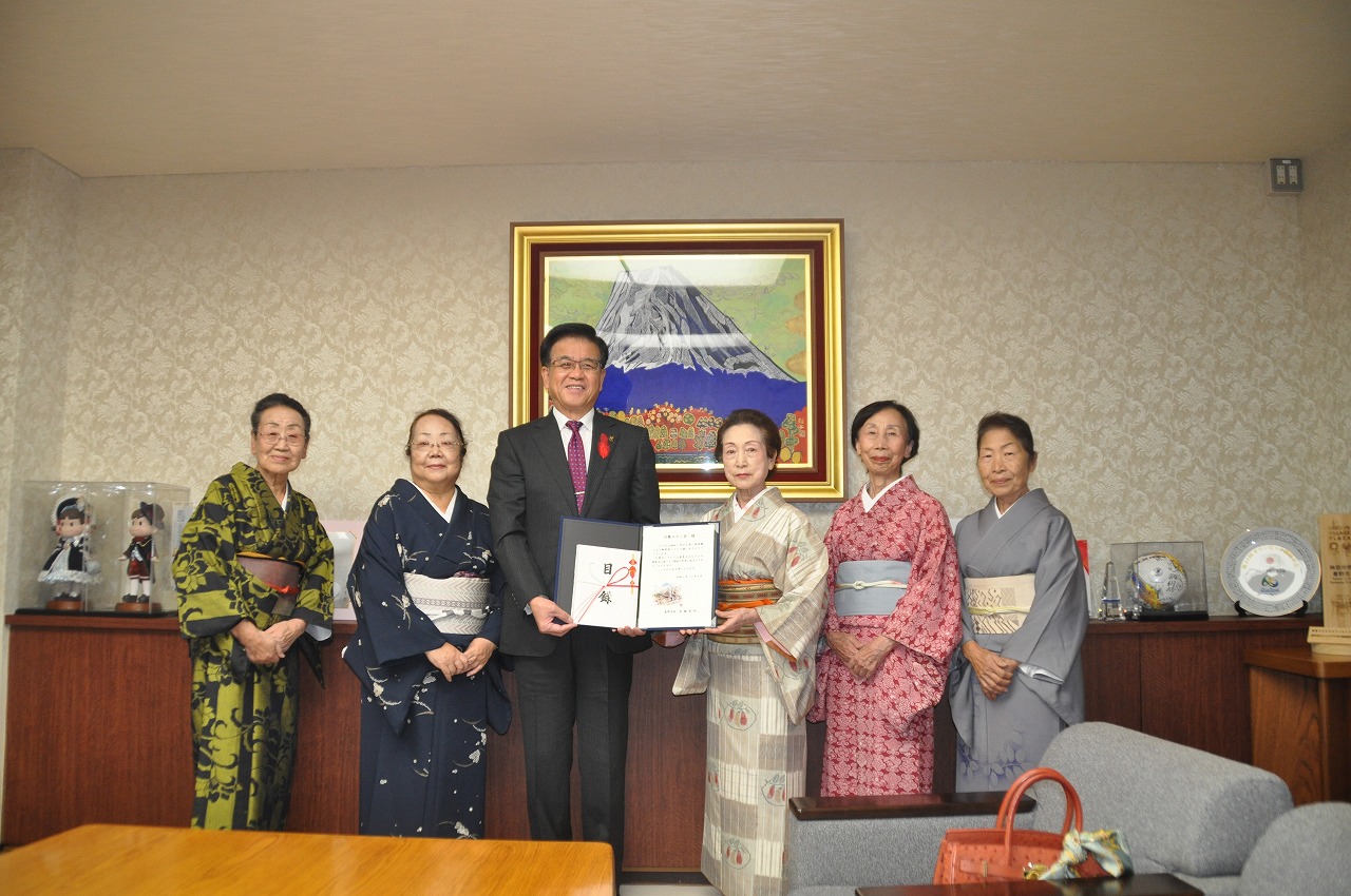 富士山の絵画を背景に、市長と着物姿の岩浅会長と関係者の女性4名が並んで立ち、寄贈を示す証書を持って笑顔で写っている記念写真