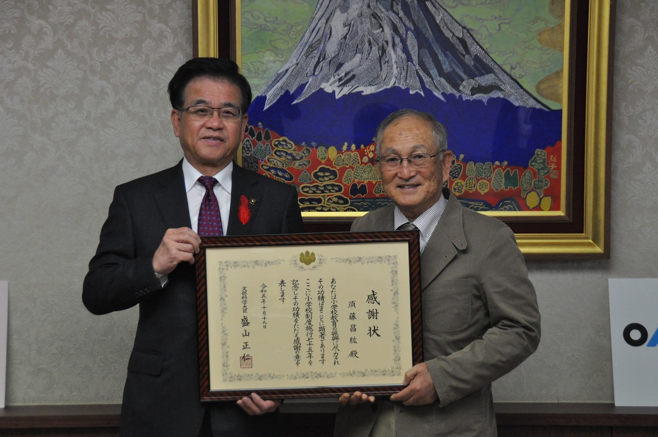富士山の絵画を背景に、市長と須藤昌紘さんが額に入った感謝状を持って、笑顔で写っている記念写真