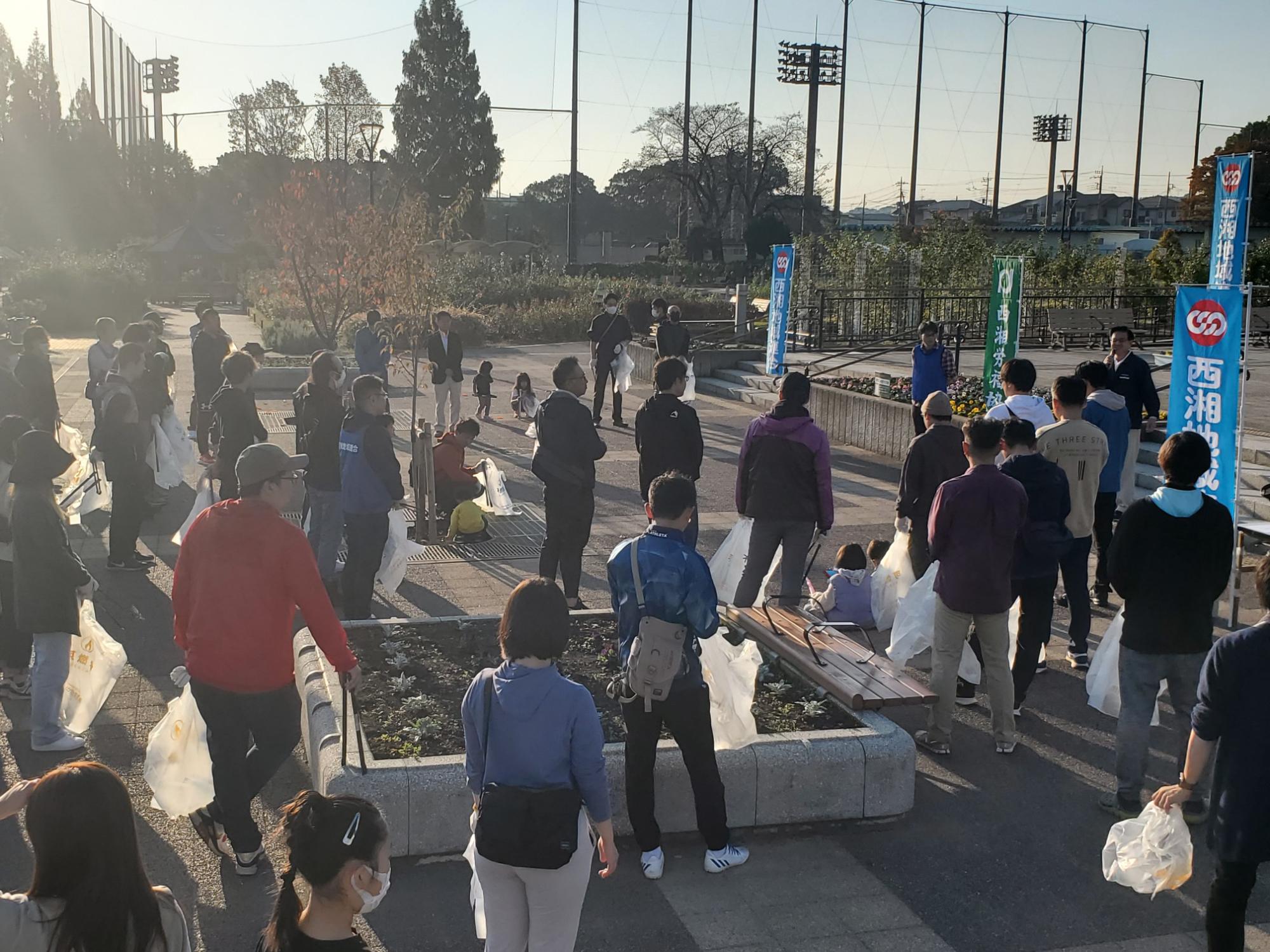 多くの人々がゴミ袋を持ち、前で市長が挨拶を行っている様子の写真