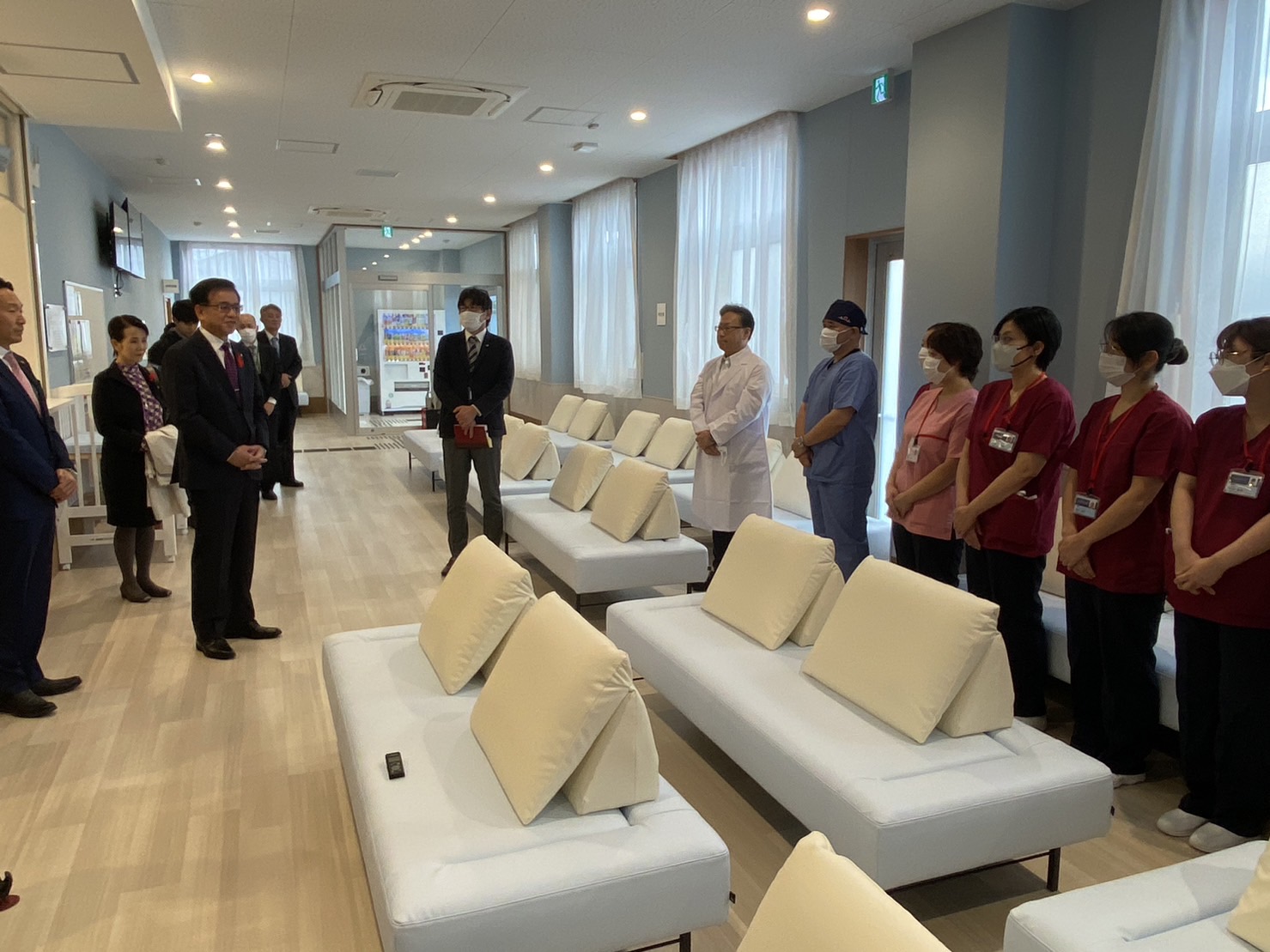長椅子が並ぶ真新しいアクアベルクリニックの待合室で、市長が医療スタッフの方々を前に挨拶をしている様子の写真