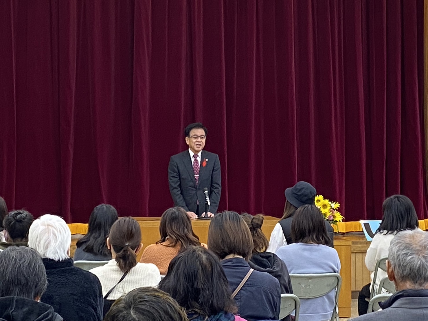 東公民館まつりの会場で、たくさんの来場者が席についており、市長が壇上のマイクの前で挨拶を行っている様子の写真