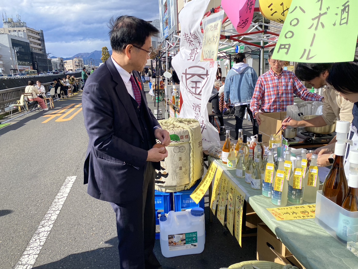 川沿いにたくさんの露店が並び、出店された酒屋の屋台で、市長が飲み物を購入している様子の写真