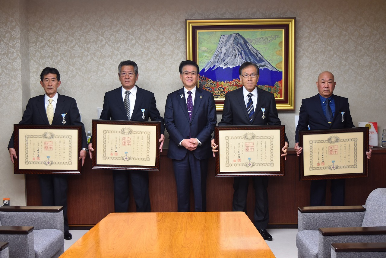 富士山の絵画を背景に、中央に立つ市長と、大きな額縁を持った4名の男性が並んで写る記念写真