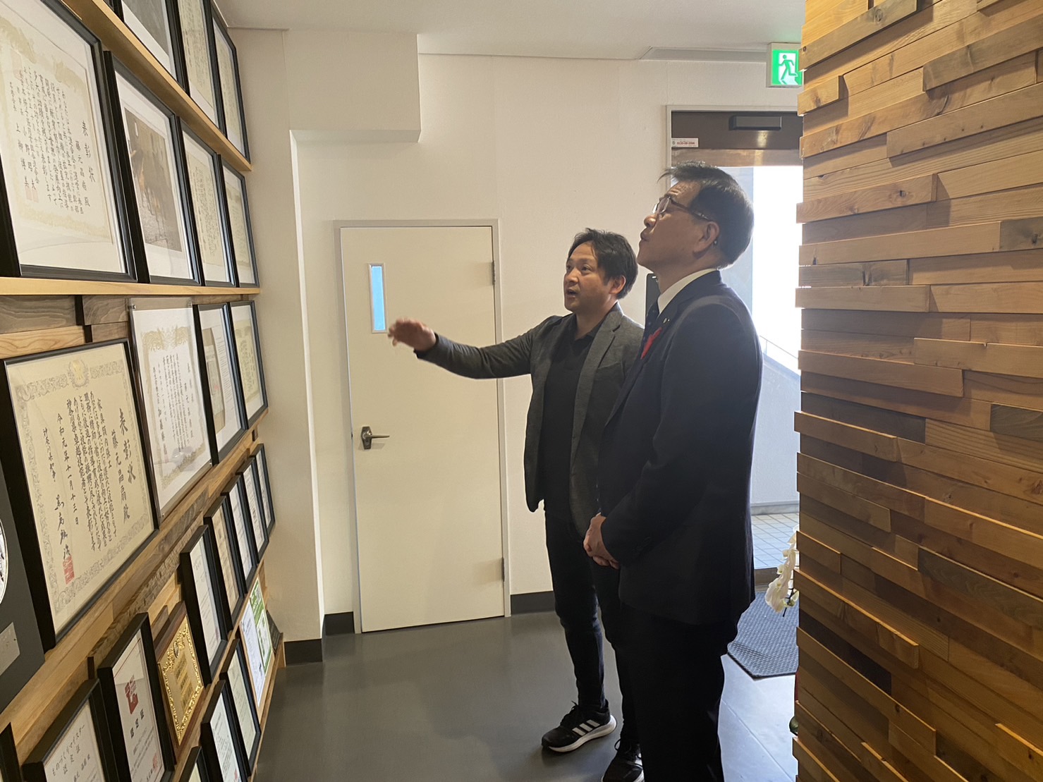 壁にたくさん賞状が入った額が飾られており、賞状額を見ながら藤元晶扇さんが高橋市長に説明をしている様子の写真