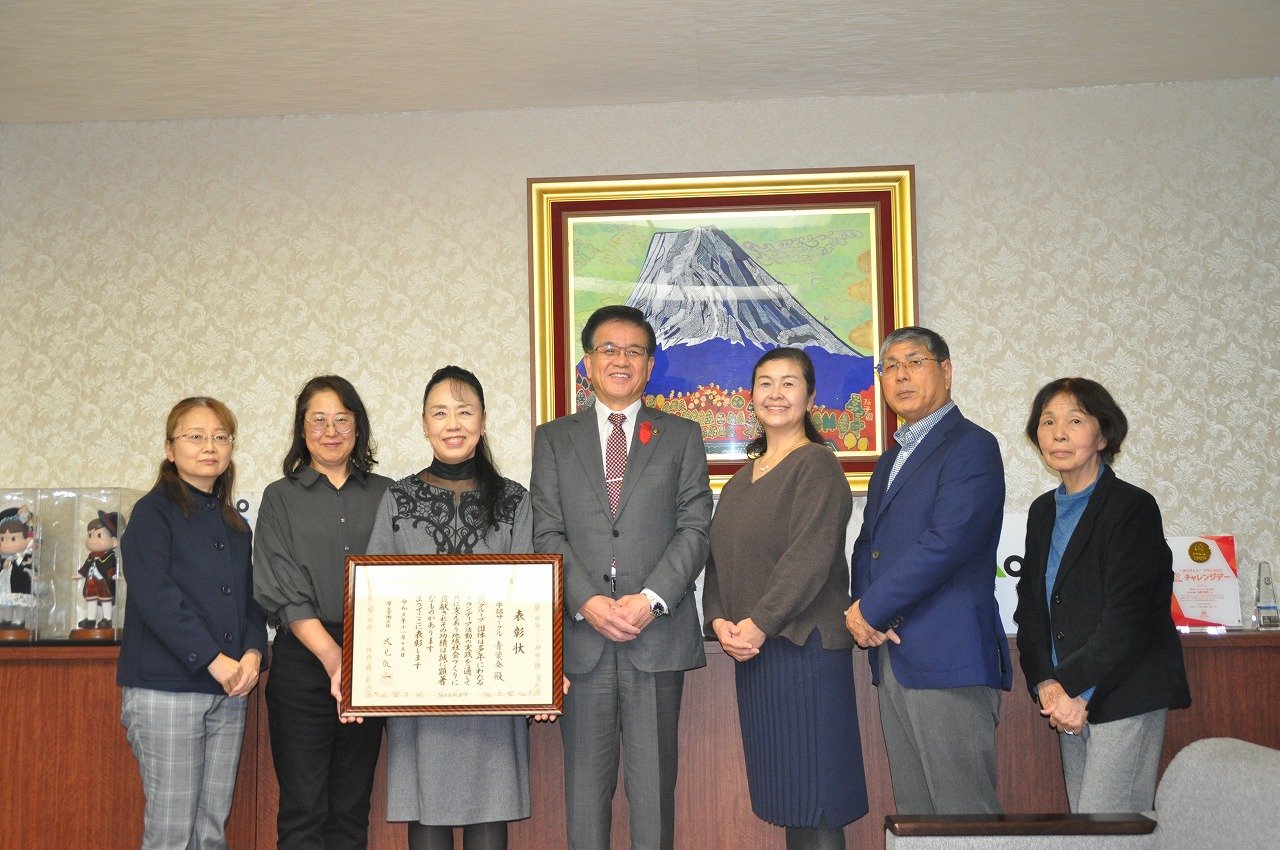 富士山の絵を背景に、賞状の入った額を手にした手話サークル青葉会の皆さんと高橋市長が並んで笑顔で写っている記念写真