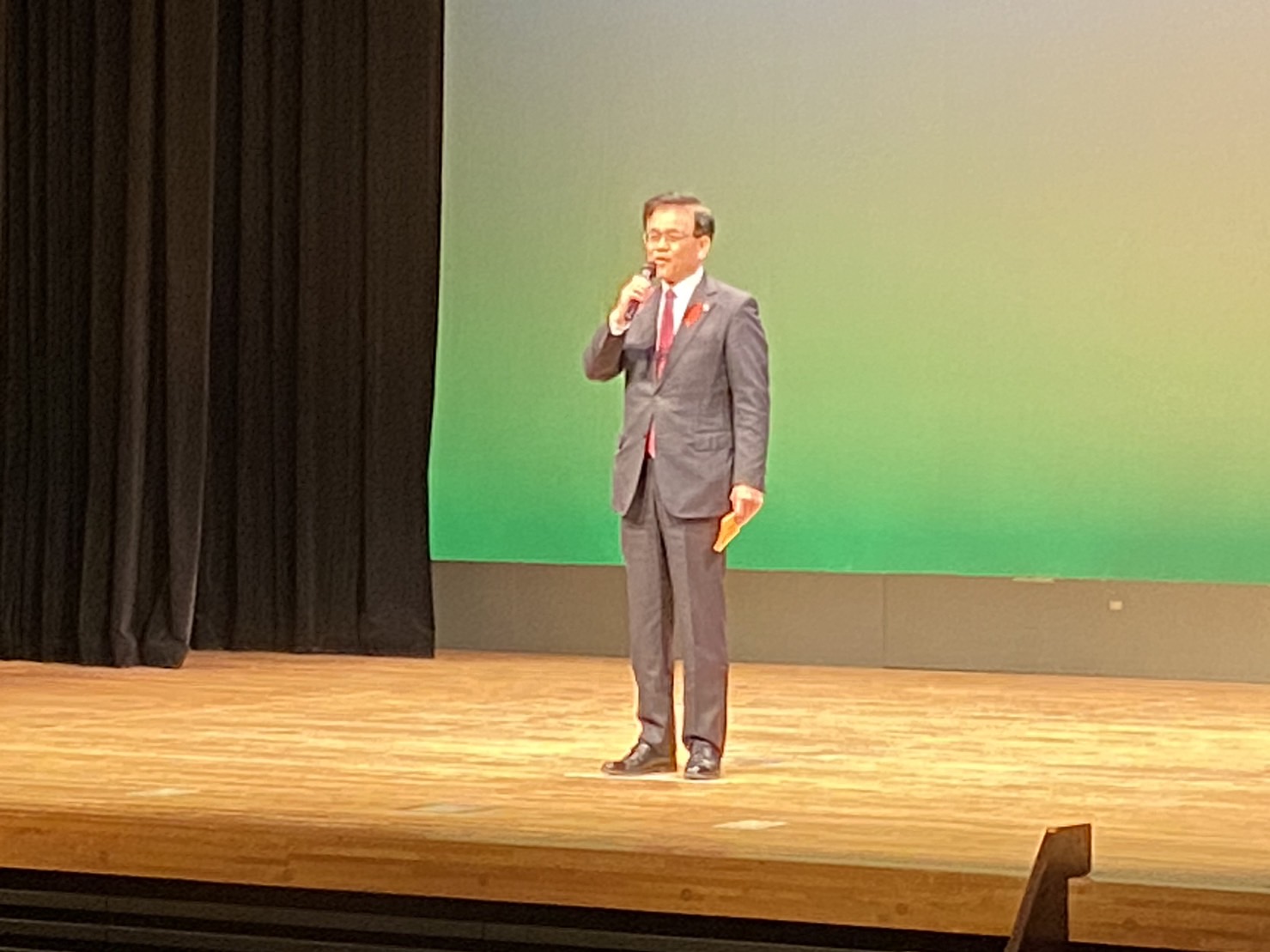 チャリティークリスマス発表会の舞台の上で市長がマイクを手に持ち、挨拶をしている様子の写真