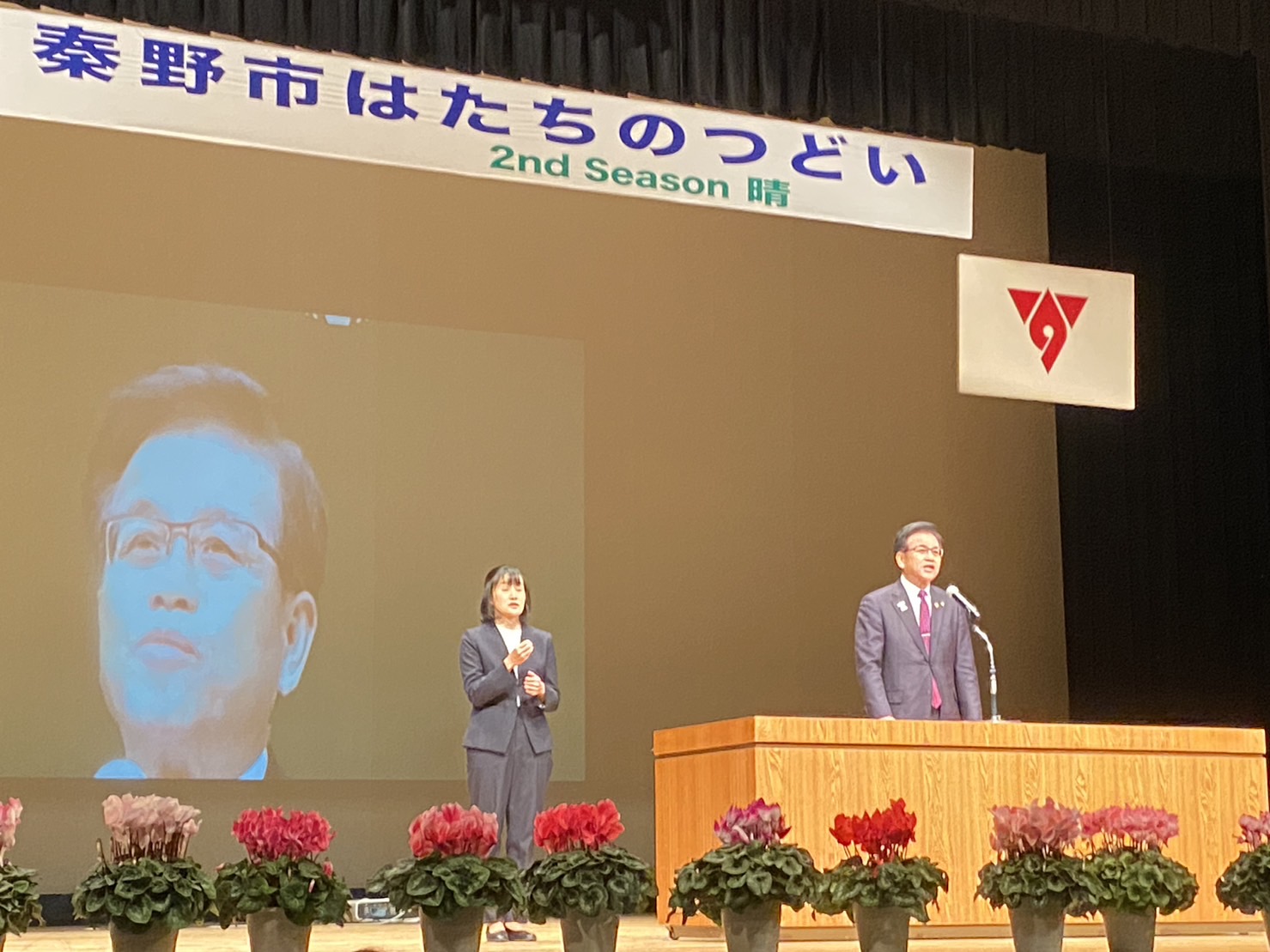 舞台上で市長が演台から挨拶し隣で女性が手話通訳を行っている写真