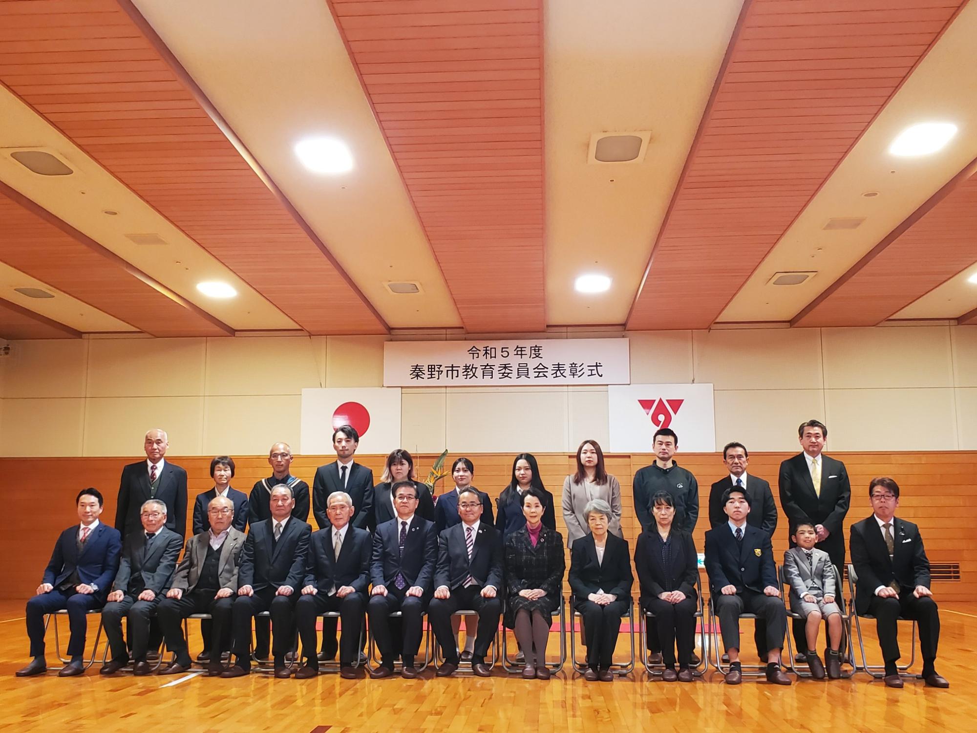 体育館で行われた令和5年度秦野市教育委員会表彰式で、受賞者や関係者が整列し記念撮影している写真