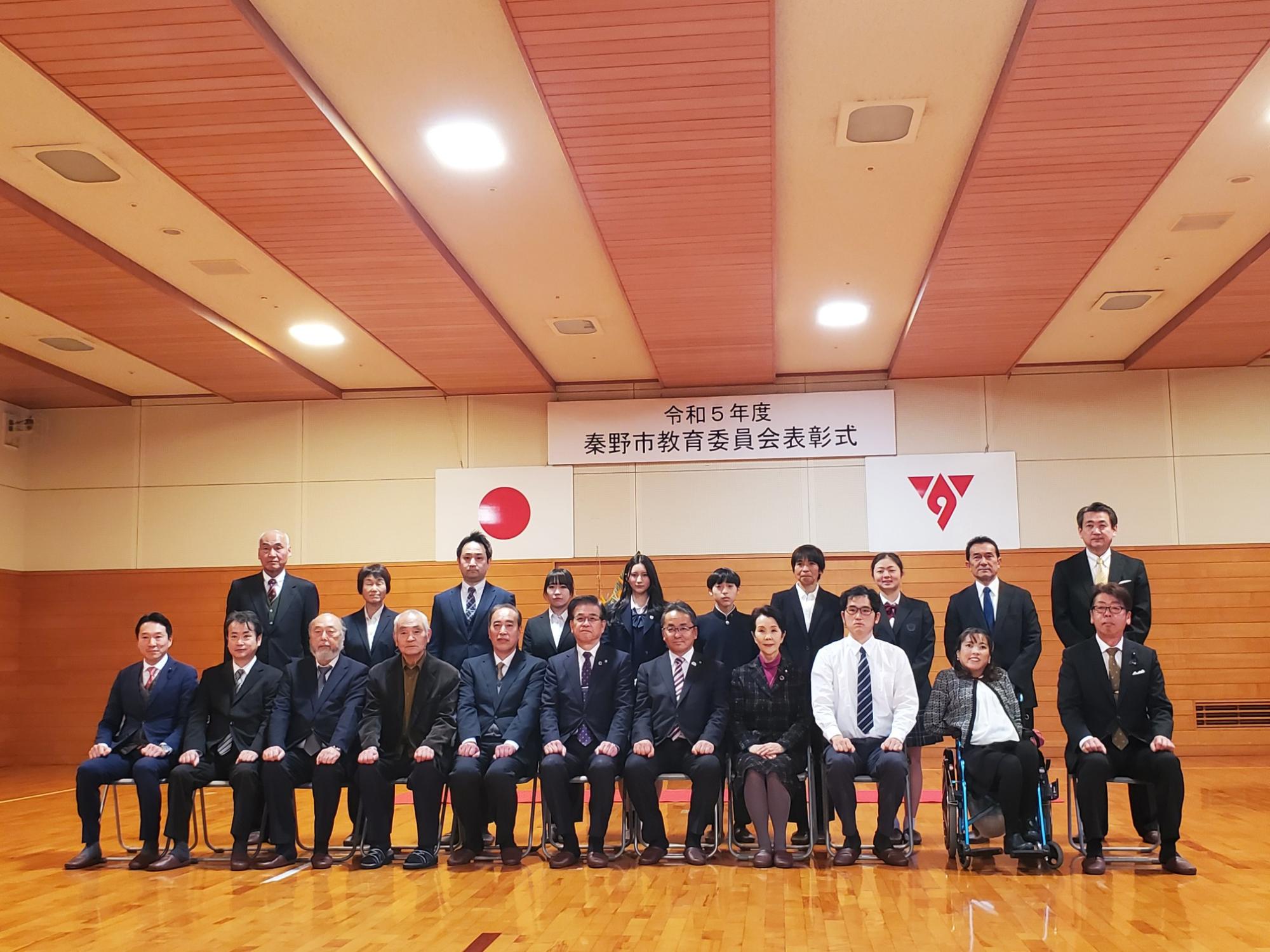 体育館で開催された令和5年度秦野市教育委員会表彰式で、受賞者や関係者が整列し記念撮影している写真