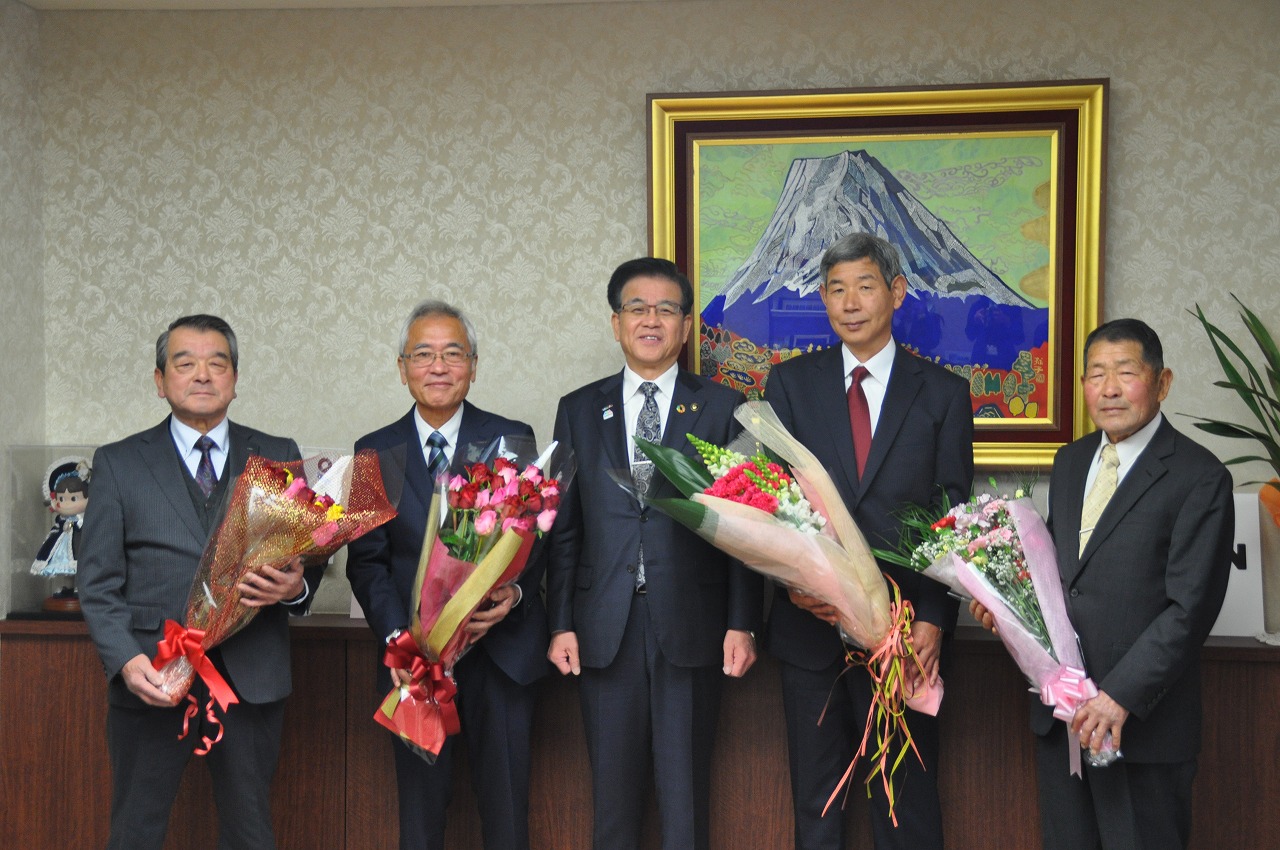 スーツ姿の男性5人が並び、中央の市長と両端を含む4人が花束を抱えて記念撮影をしている写真
