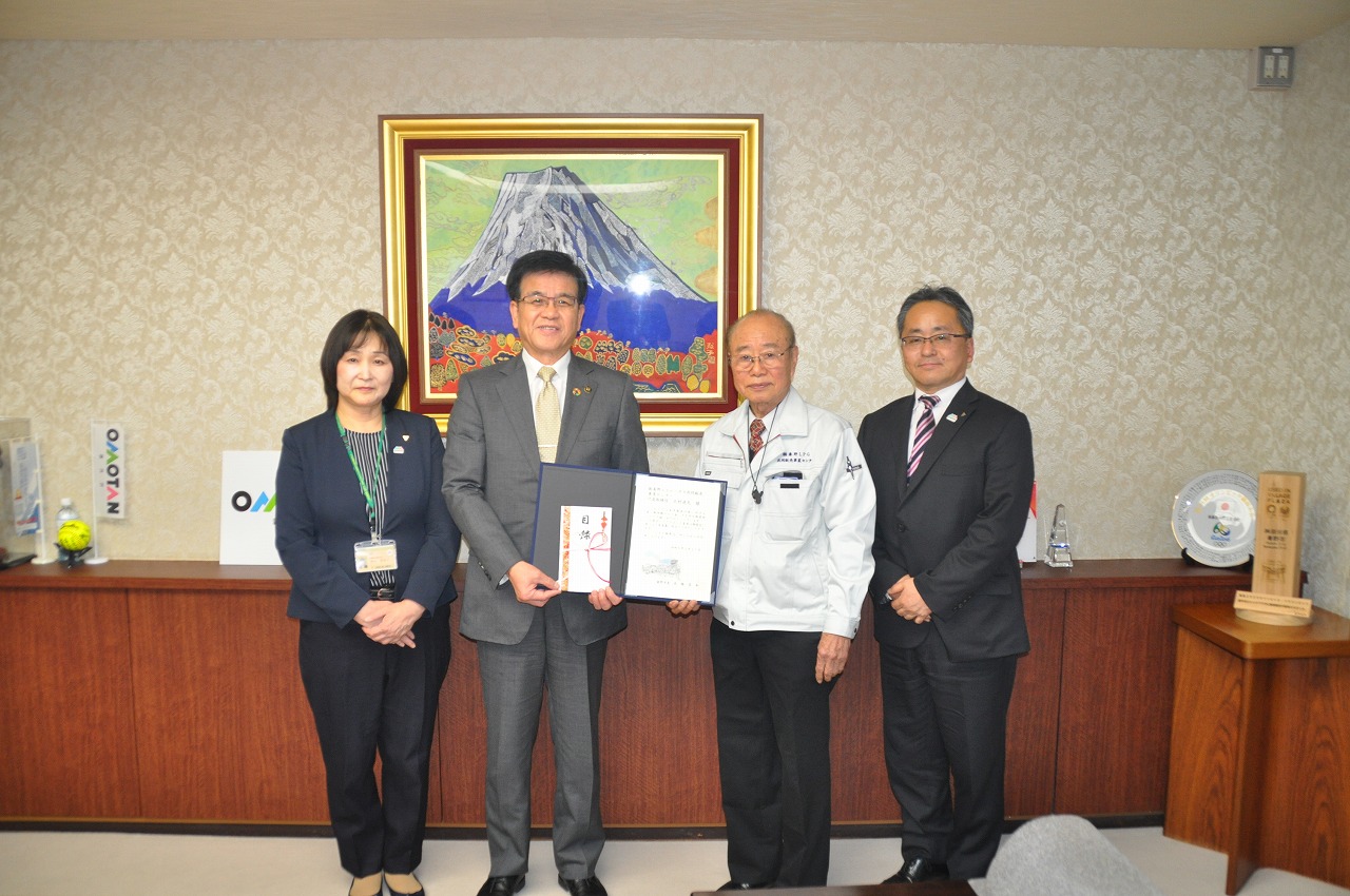 市長と北村代表取締役が一緒に賞状を手に持ち、その両サイドに関係者方が立ち横に並んで記念撮影している写真