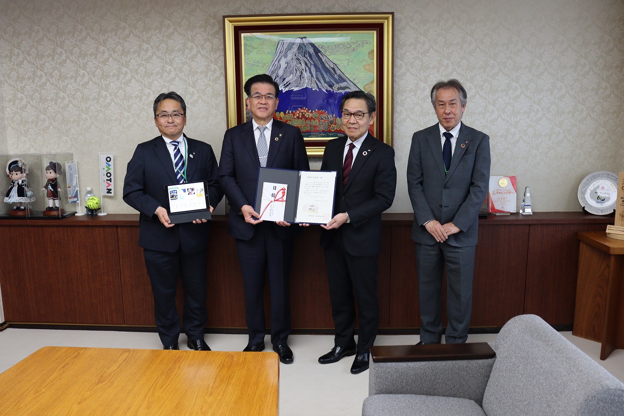 平塚信用金庫の方々が横一列に並び、市長と三簾常務理事が証書や記念品を持って記念撮影している写真