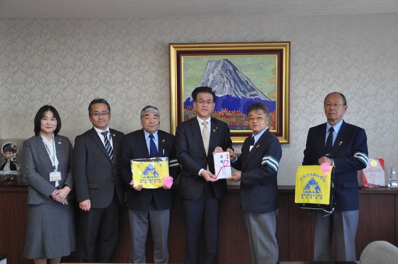 秦野市交通安全協会の方々が横一列に並び、市長と古谷会長がご祝儀袋を、他の方々が黄色いカバーをつけたランドセルを持って記念撮影している写真