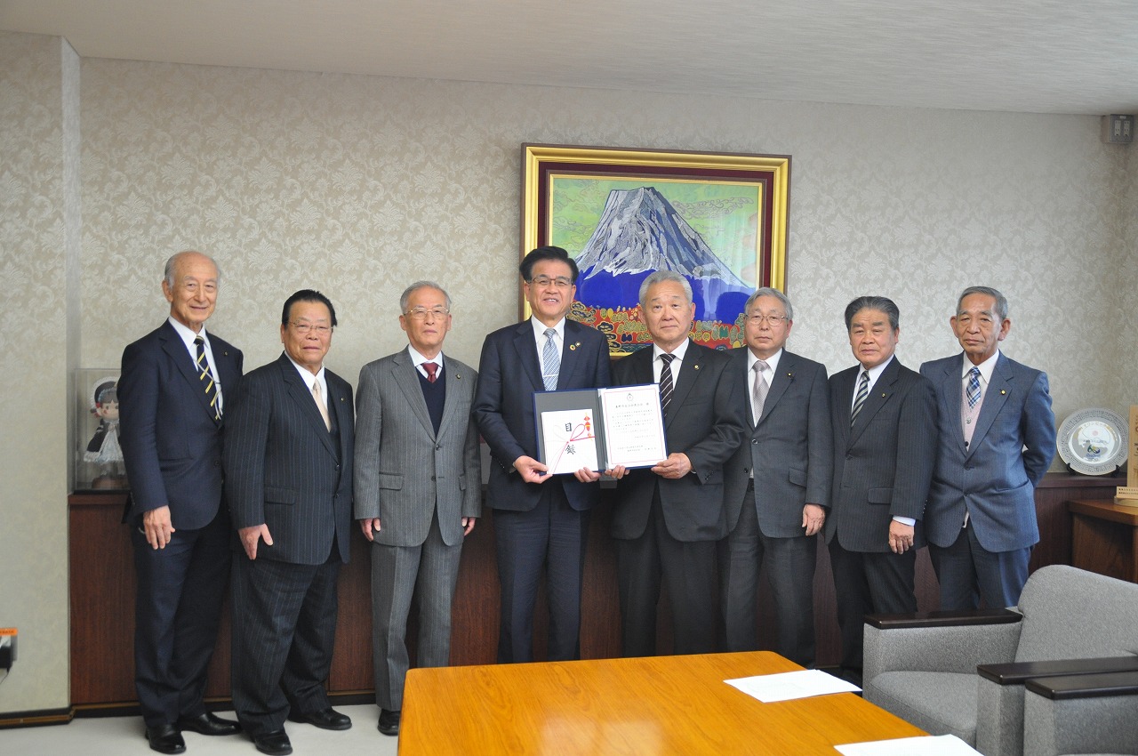 秦野市自治会連合会の方々が横一列に並び、市長と岩崎会長が証書を開いて見せながら記念撮影している写真