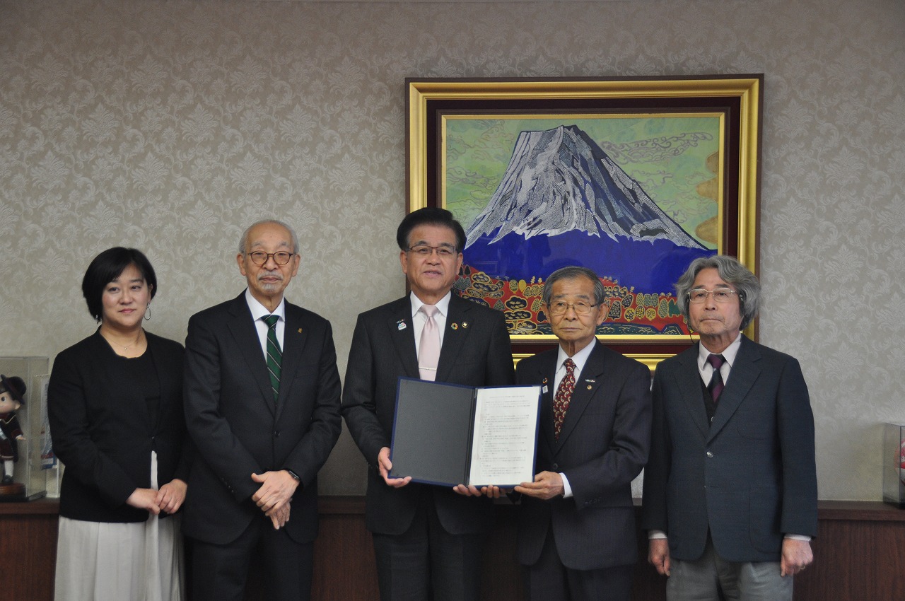 特定非営利活動法人みんなの食堂の方々が横一列に並び、中央の市長と代表の方と二人で証書を開いて見せながら記念撮影している写真