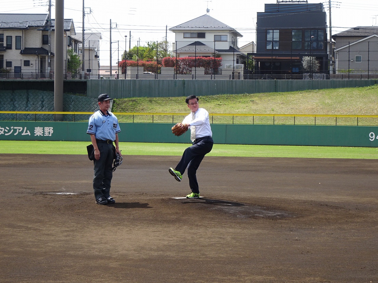 ワイシャツ姿の市長がマウンドから投球する様子を、横で審判が見ている様子の写真