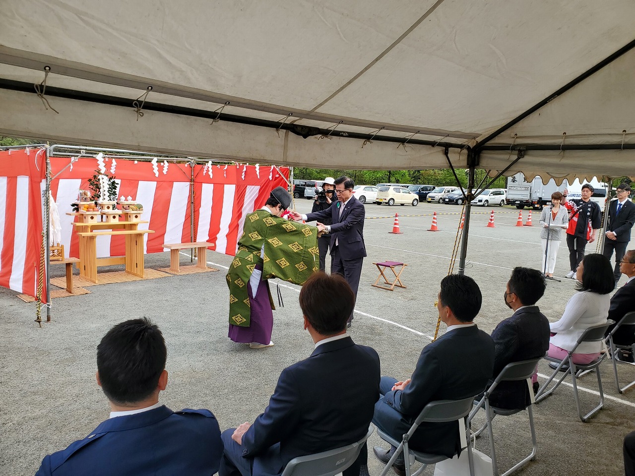 祭壇の前で神主とスーツ姿の市長が向き合い儀式に臨み、その様子をテント内に設けられた椅子に関係者が座って見ている写真