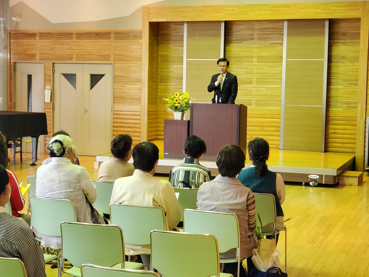 壇上の演台に立ったスーツ姿の市長がマイクで話す前方の客席に参加者が座り話を聞いている様子の写真