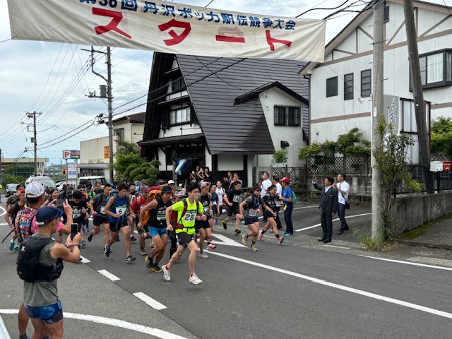 「第36回丹沢ボッカ駅伝競走大会」と書かれた横断幕の下で、ゼッケンをつけた大勢のランナーたちが一斉にスタートしている様子の写真
