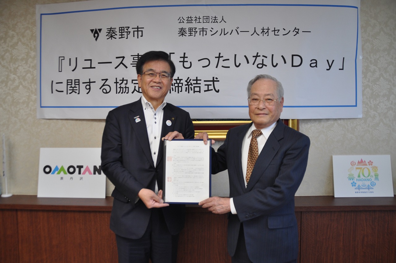 「リユース事業『もったいないDay』に関する協定」と書かれた看板の前で、スーツ姿の市長と男性が協定書を並んで持っている様子の写真