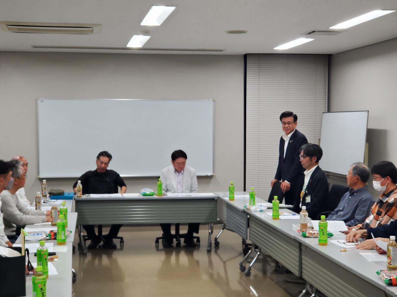 白板のある会議室で、市長が立って発言し、関係者が聞いている様子の写真