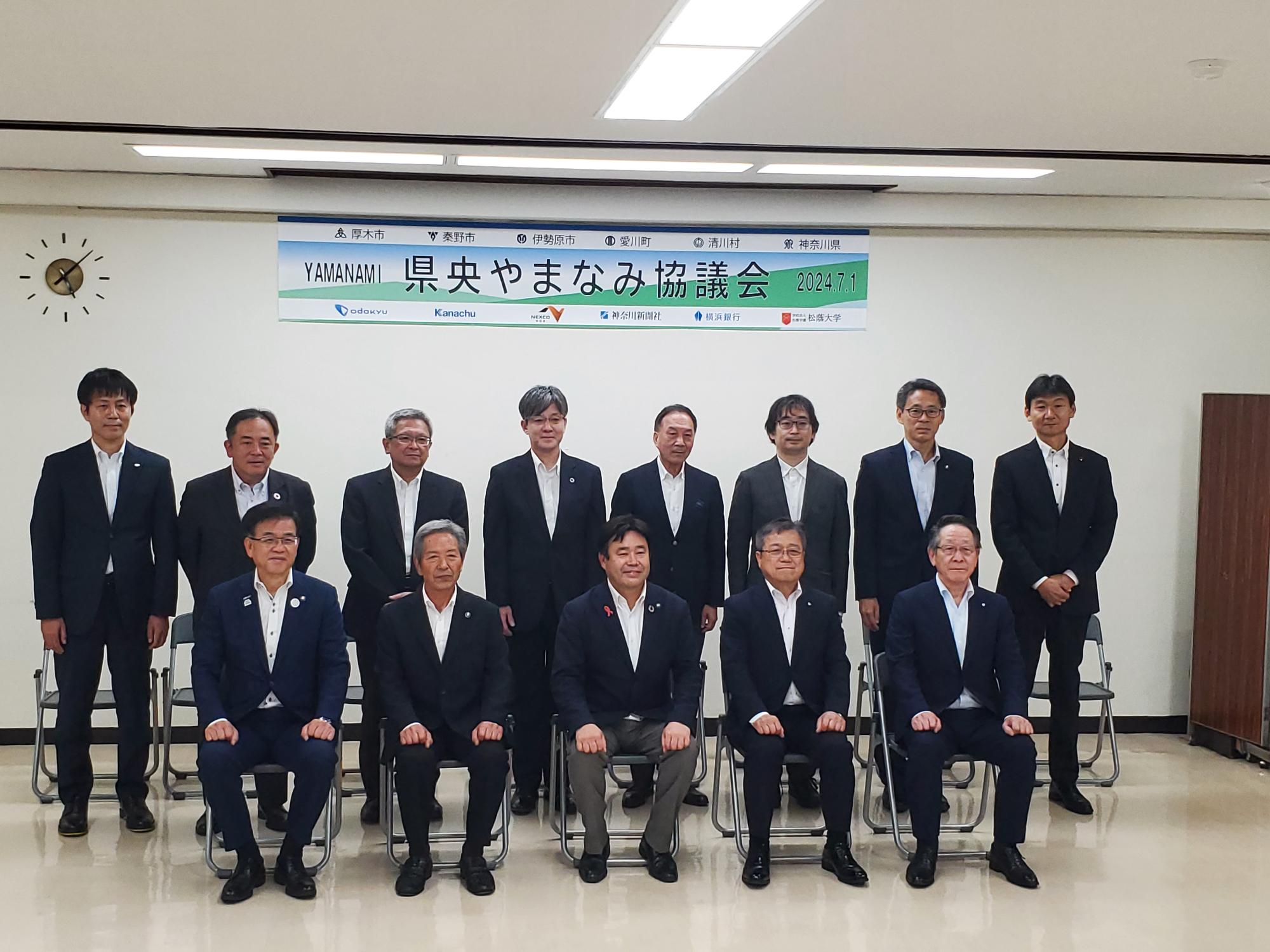 「県央やまなみ協議会」の横断幕の下で、市長と関係者たちがスーツ姿で整列し、正面を向いている集合写真